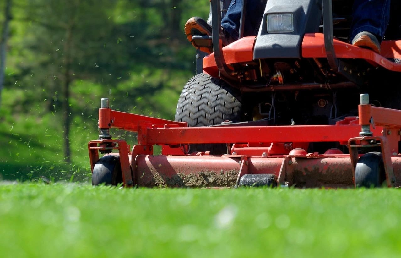 A person on a red lawn mower in the grass.